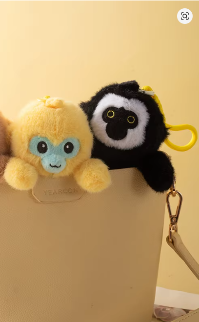 Two plush keychains, one yellow and one black and white, attached to a beige handbag.