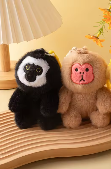 Two plush toys, one black and white and one brown with a pink face, sitting on a wooden surface.