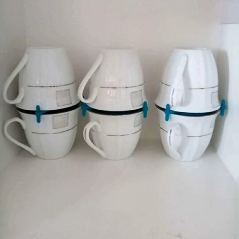 Three white ceramic mugs stacked horizontally with blue handles and black bands, displayed on a white shelf.