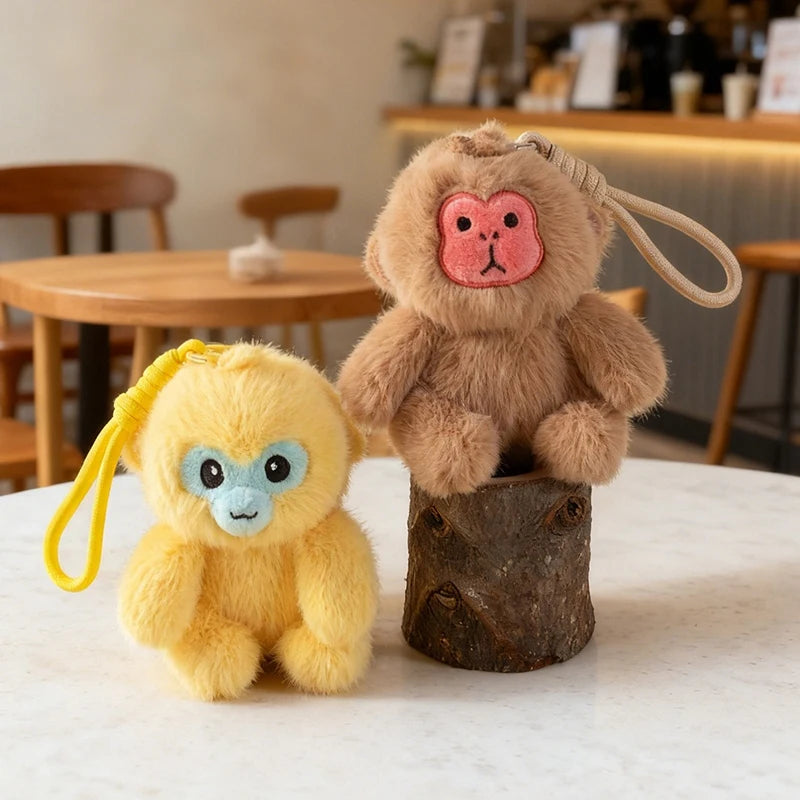 Two plush monkey toys, one yellow and one brown, on a white surface with a blurred indoor background.