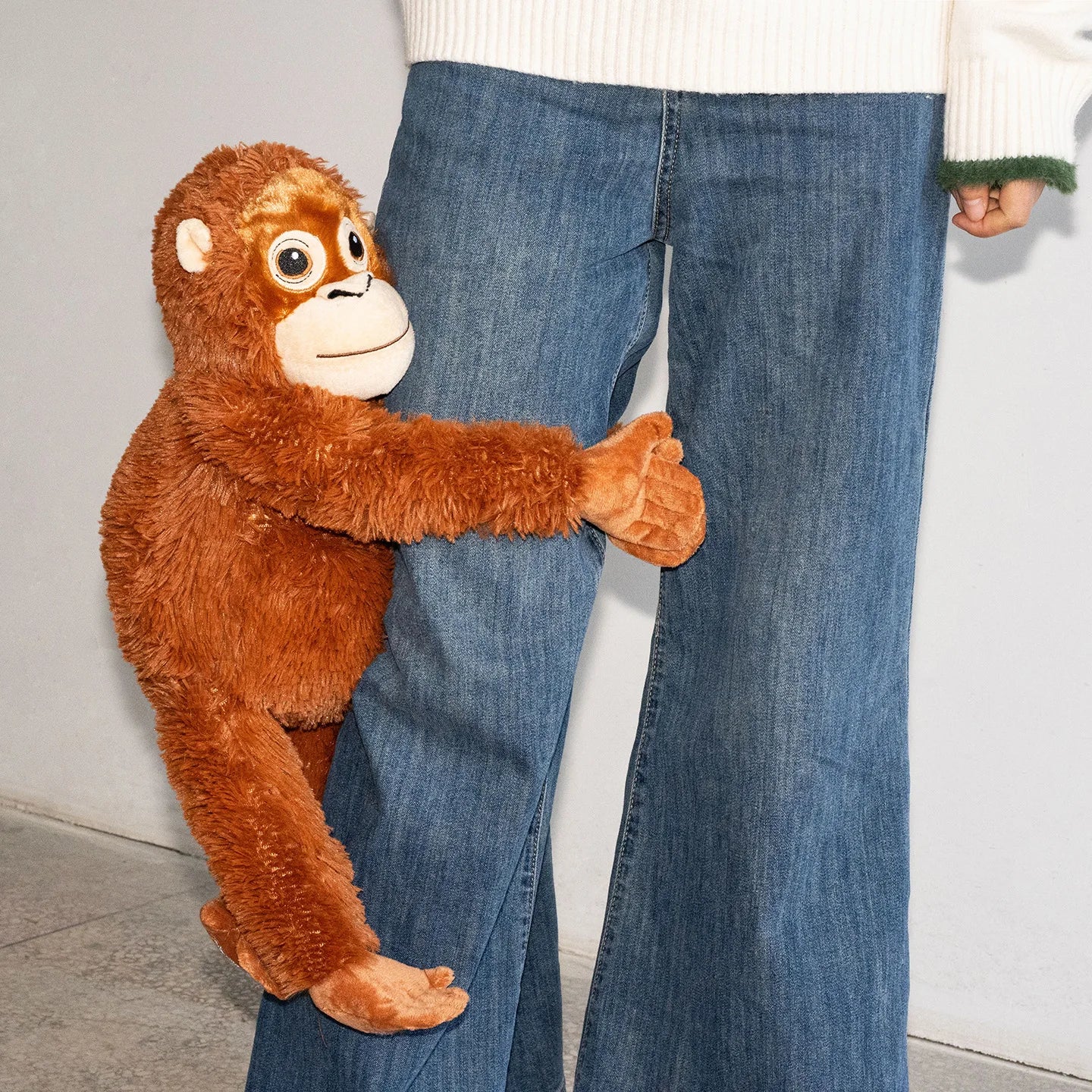 Stuffed monkey toy interacting with a person wearing blue jeans against a neutral background