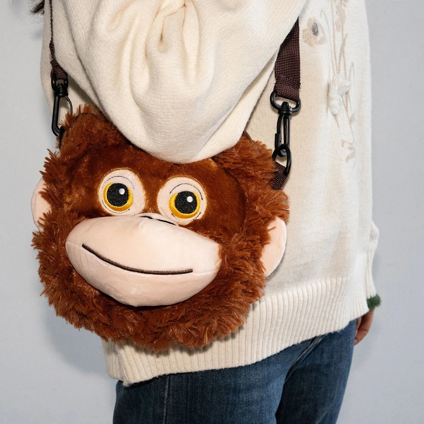 Person wearing a white sweater with a monkey-shaped pouch on a plain background