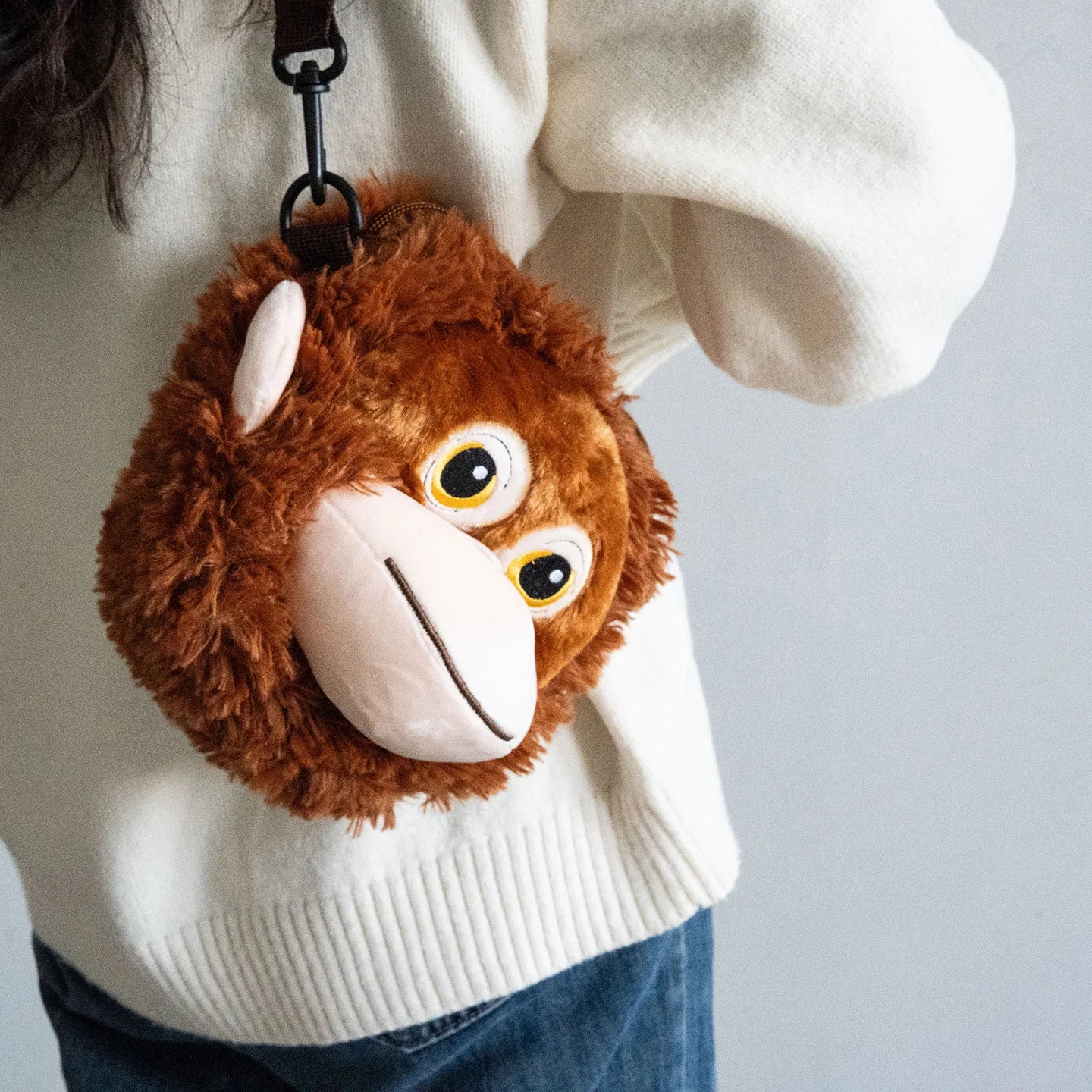 Plush monkey keychain attached to a white sweater on a gray background