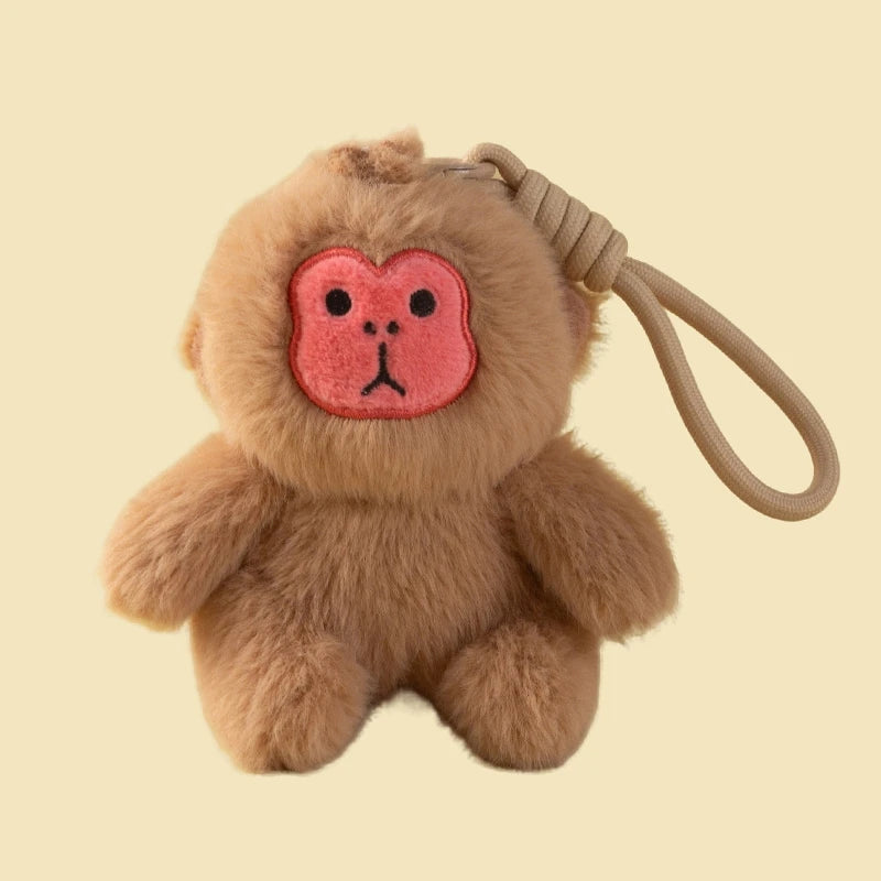 Brown plush monkey keychain with a pink face on a beige background