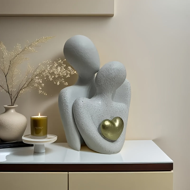 Abstract sculpture of two figures embracing with a heart on a shelf, next to a candle and vase.
