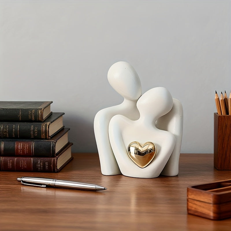 White ceramic sculpture of two figures embracing with a gold heart on a wooden surface.